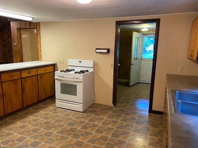 kitchen featuring wood walls, white range with gas stovetop, and sink