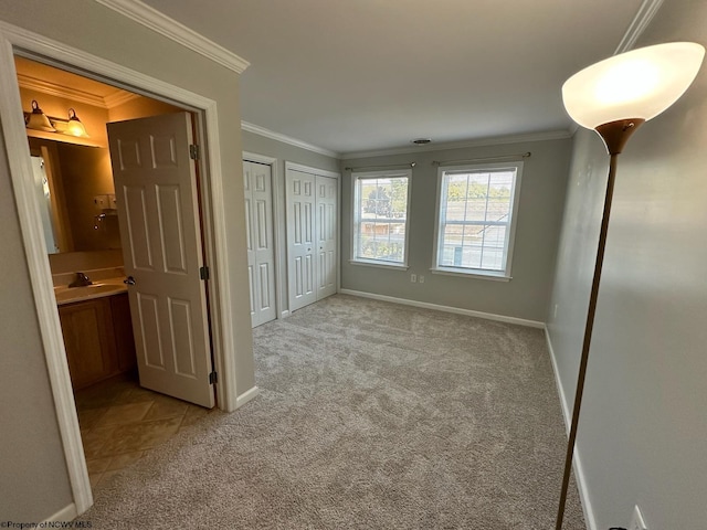 unfurnished bedroom featuring crown molding, connected bathroom, two closets, and light carpet