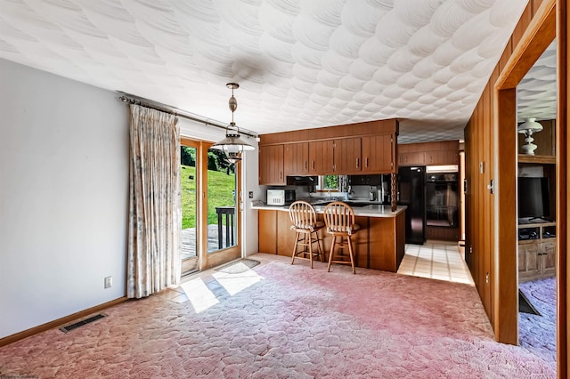 kitchen with black fridge, kitchen peninsula, decorative light fixtures, light carpet, and a breakfast bar area