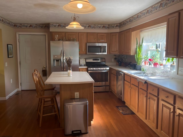 kitchen with stainless steel appliances, decorative light fixtures, a center island, hardwood / wood-style flooring, and sink