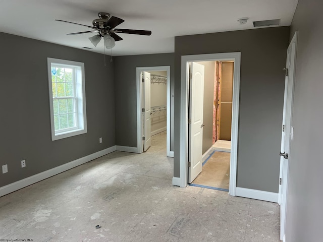 unfurnished bedroom featuring a spacious closet, ensuite bath, ceiling fan, and a closet