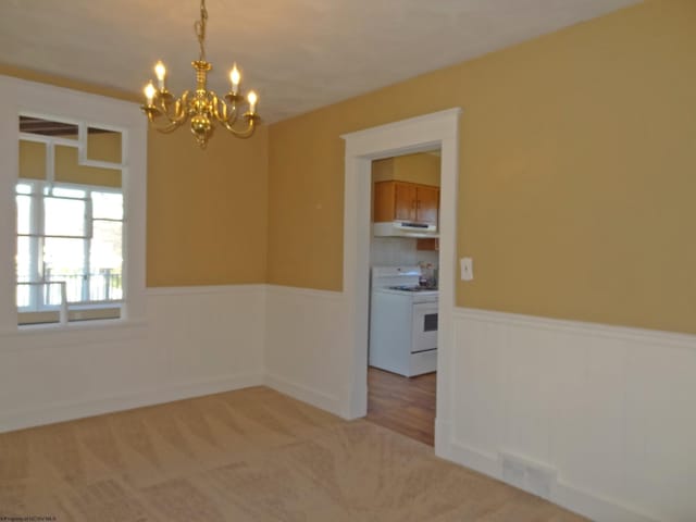 empty room with light colored carpet and a notable chandelier