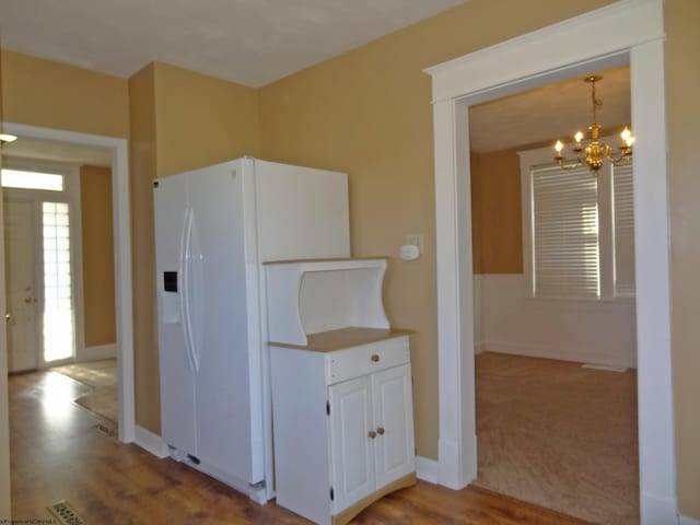 kitchen with hanging light fixtures, light hardwood / wood-style floors, white refrigerator with ice dispenser, white cabinets, and a chandelier