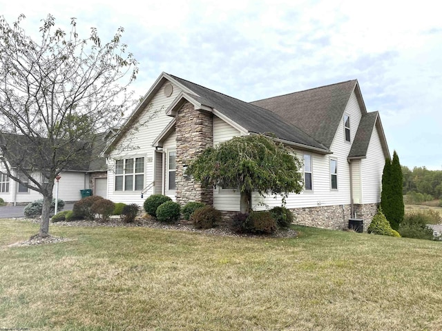 view of side of home with a yard, a shingled roof, and stone siding
