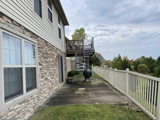 view of side of property featuring stairway, fence, a patio, a wooden deck, and stone siding