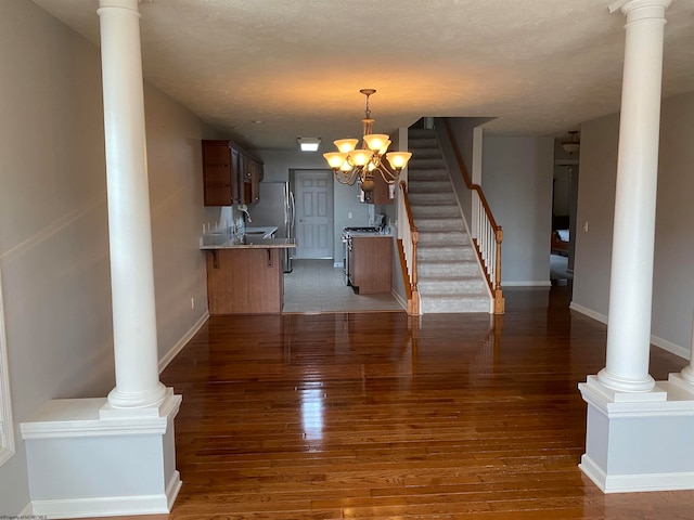 unfurnished living room with a notable chandelier, decorative columns, and dark hardwood / wood-style flooring