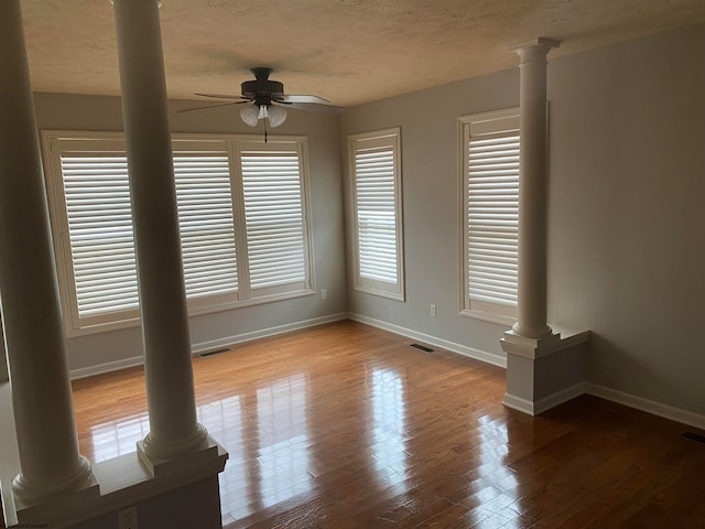 unfurnished room featuring a healthy amount of sunlight, light hardwood / wood-style flooring, ceiling fan, and ornate columns