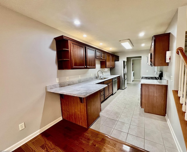 kitchen featuring recessed lighting, stainless steel appliances, open shelves, light countertops, and a sink