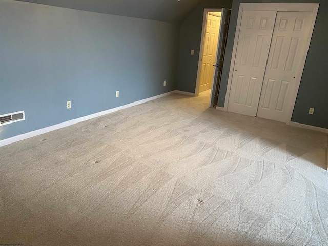 unfurnished bedroom with a closet, light carpet, baseboards, visible vents, and lofted ceiling