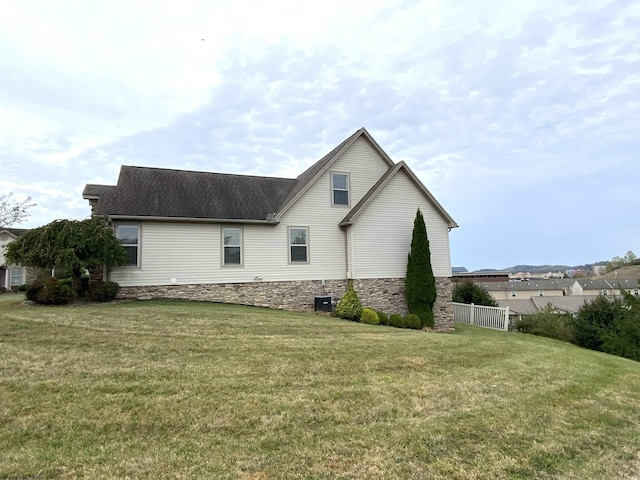 view of side of property with a lawn, stone siding, and roof with shingles