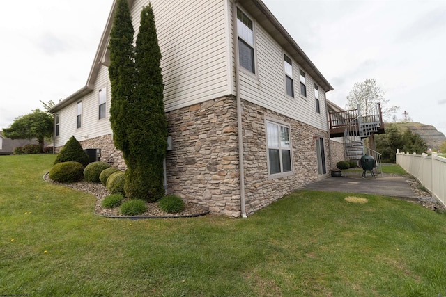 view of side of property featuring a lawn, stairway, a patio area, and stone siding