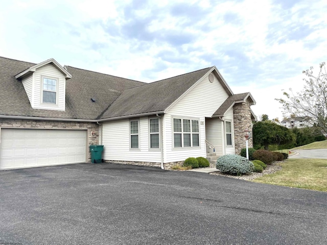 view of front of property with driveway, roof with shingles, and stone siding