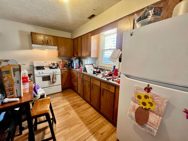 kitchen featuring a textured ceiling, light wood-type flooring, and white appliances