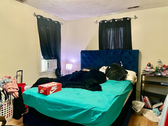 bedroom with cooling unit, a textured ceiling, and hardwood / wood-style floors