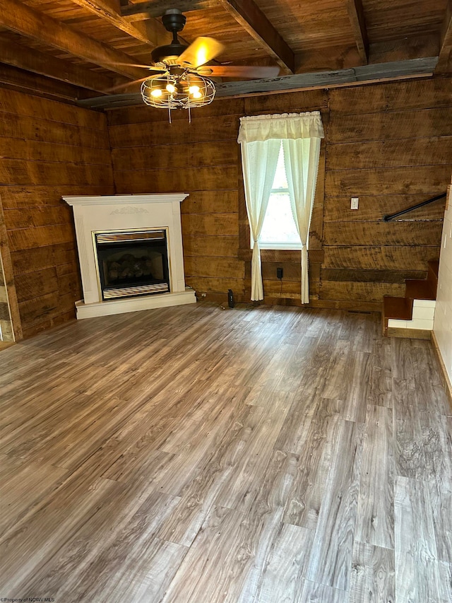 unfurnished living room featuring wood ceiling, wood-type flooring, beam ceiling, wood walls, and ceiling fan