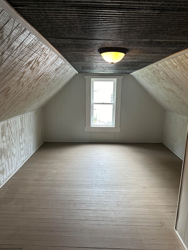 additional living space featuring lofted ceiling, wooden walls, and hardwood / wood-style flooring