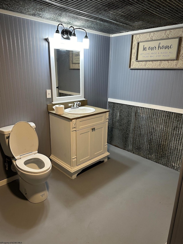 bathroom with concrete flooring, vanity, wooden walls, and toilet