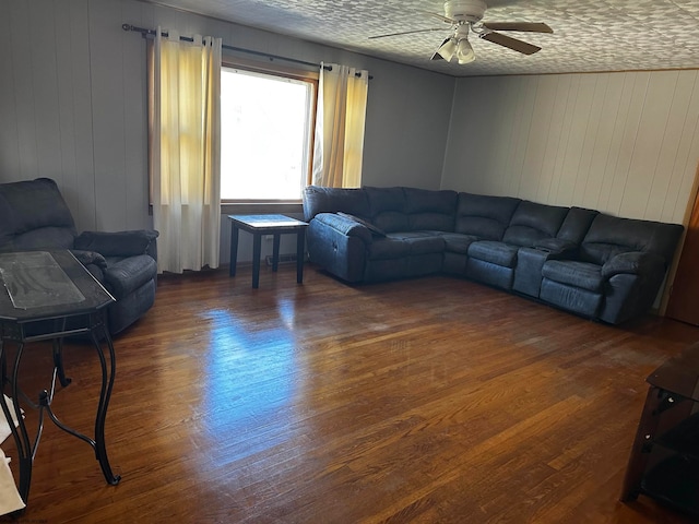 living room featuring ceiling fan, a textured ceiling, wood walls, and dark wood-type flooring