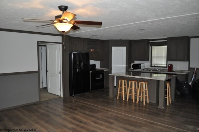 kitchen featuring ceiling fan, a kitchen island, wood-type flooring, black appliances, and a breakfast bar area