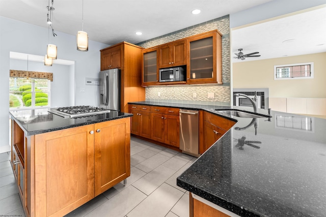 kitchen with appliances with stainless steel finishes, hanging light fixtures, dark stone counters, ceiling fan, and a center island with sink