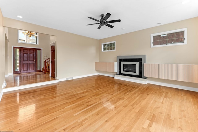 unfurnished living room with ceiling fan with notable chandelier and light hardwood / wood-style flooring