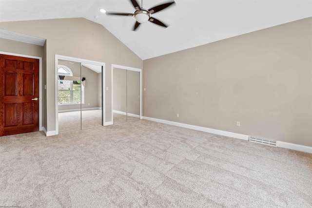 unfurnished bedroom with lofted ceiling, multiple closets, ceiling fan, and light colored carpet