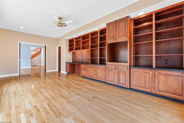 unfurnished living room with built in desk, ceiling fan, and light hardwood / wood-style floors