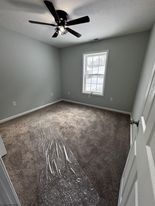 spare room featuring a textured ceiling, ceiling fan, and dark carpet