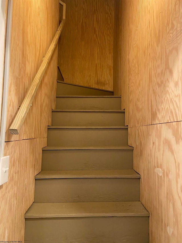 stairway featuring wooden walls