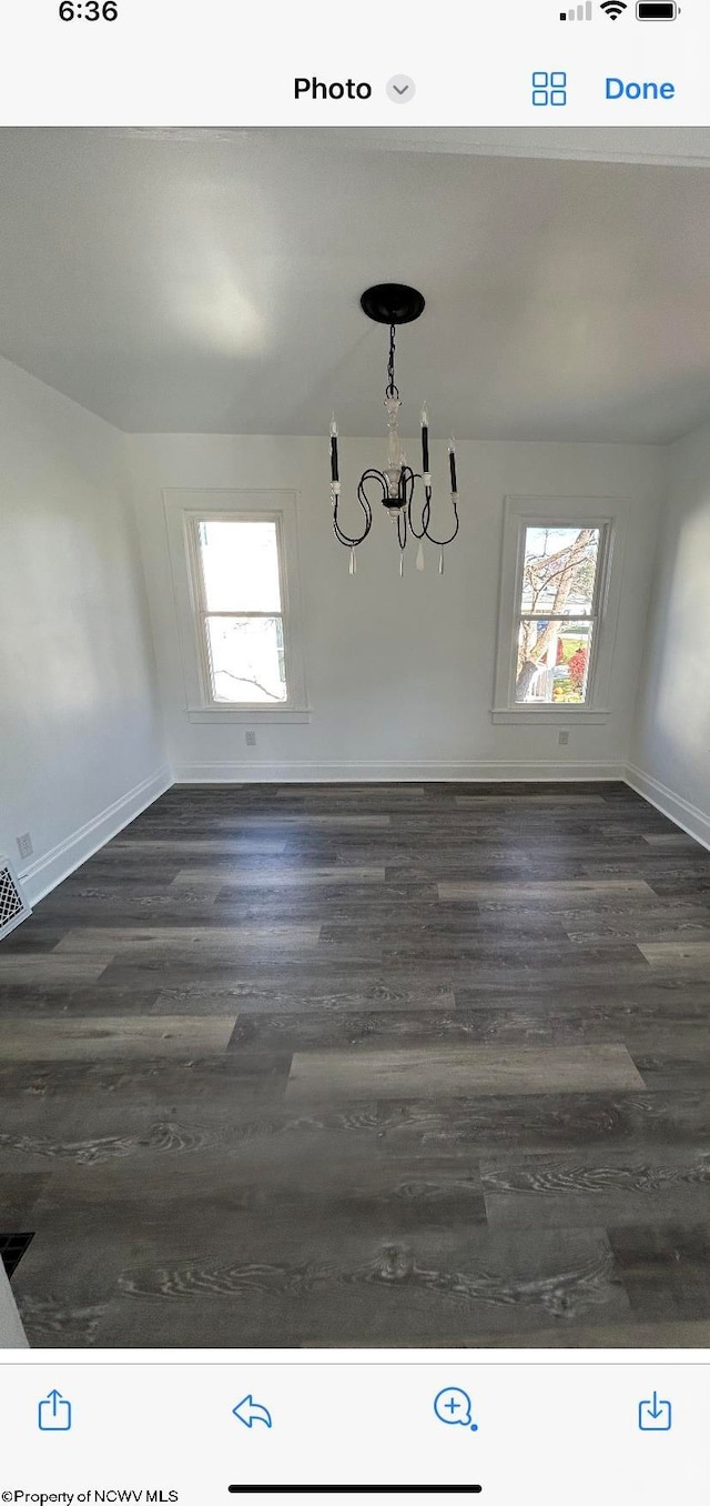 unfurnished room with an inviting chandelier and dark hardwood / wood-style flooring