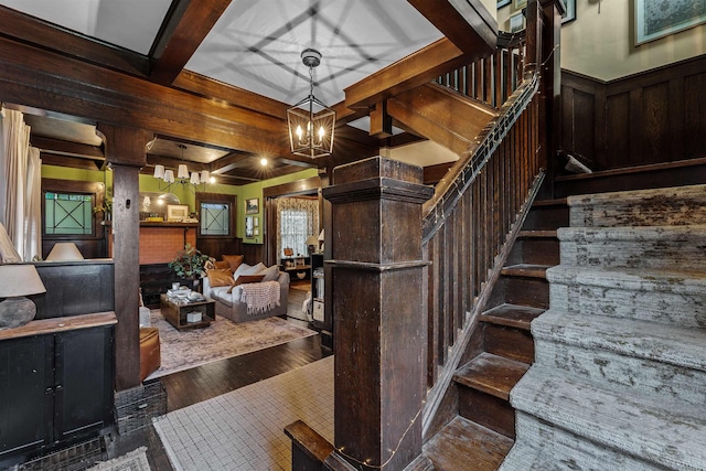 staircase with wood walls, beam ceiling, an inviting chandelier, decorative columns, and hardwood / wood-style floors