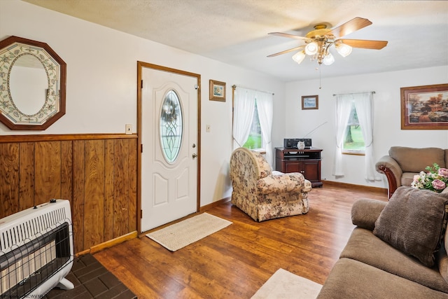 foyer with heating unit, a textured ceiling, wooden walls, hardwood / wood-style floors, and ceiling fan