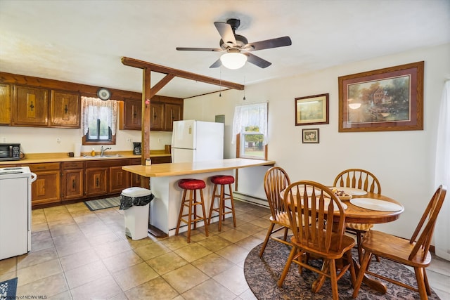 kitchen featuring ceiling fan, sink, white appliances, a baseboard heating unit, and a breakfast bar area