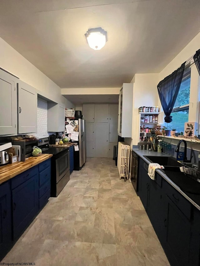 kitchen with butcher block countertops, appliances with stainless steel finishes, sink, and white cabinetry