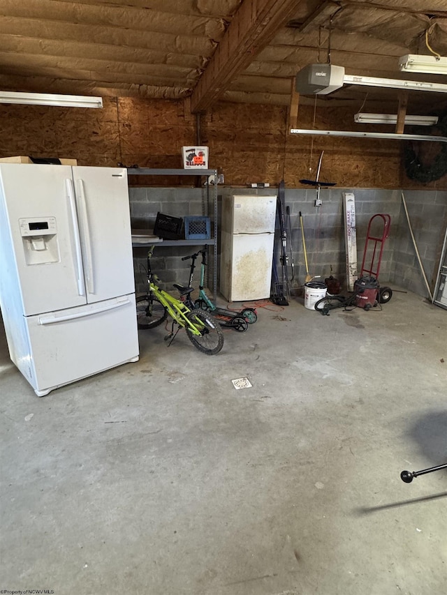 garage with concrete block wall, white fridge with ice dispenser, freestanding refrigerator, and a garage door opener