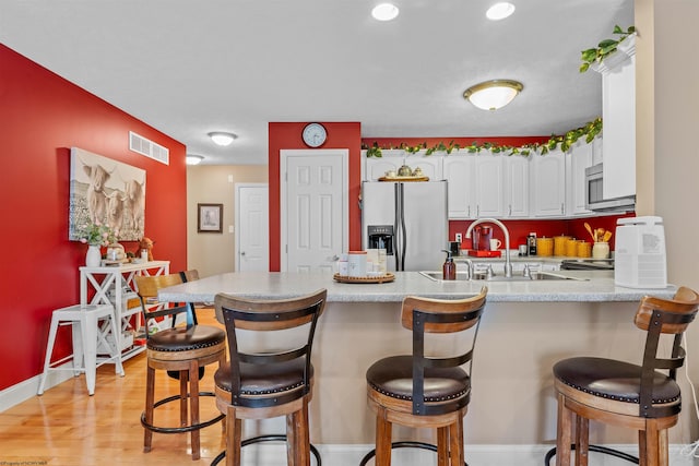 kitchen with sink, kitchen peninsula, white cabinetry, stainless steel appliances, and light wood-type flooring