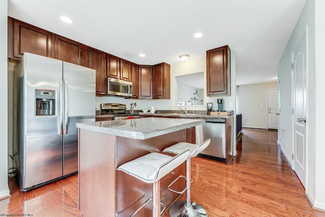 kitchen featuring a breakfast bar, stainless steel appliances, a center island, light hardwood / wood-style flooring, and sink