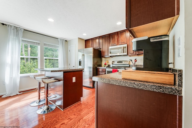 kitchen featuring a breakfast bar, a textured ceiling, a kitchen island, light hardwood / wood-style flooring, and appliances with stainless steel finishes