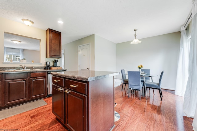 kitchen with a kitchen island, wood-type flooring, decorative light fixtures, stainless steel dishwasher, and sink