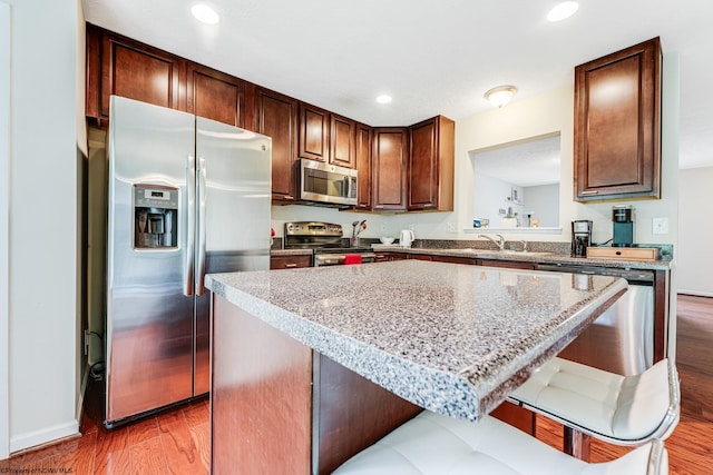 kitchen featuring appliances with stainless steel finishes, a kitchen island, dark hardwood / wood-style floors, and a breakfast bar