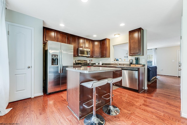 kitchen featuring sink, a kitchen island, appliances with stainless steel finishes, a kitchen breakfast bar, and hardwood / wood-style floors