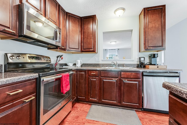 kitchen featuring a textured ceiling, appliances with stainless steel finishes, light wood-type flooring, and sink