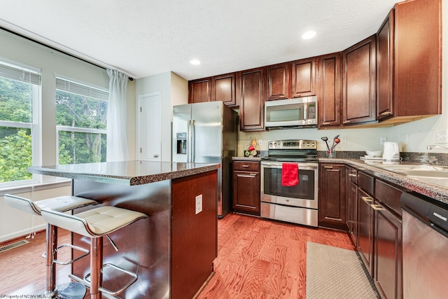 kitchen featuring appliances with stainless steel finishes, light hardwood / wood-style floors, a textured ceiling, a kitchen bar, and sink