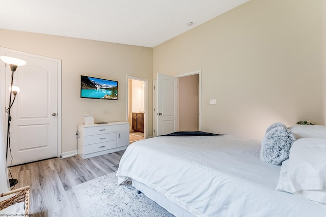 bedroom with light hardwood / wood-style flooring, connected bathroom, and vaulted ceiling