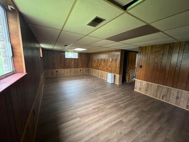 basement with a healthy amount of sunlight, a drop ceiling, wooden walls, and hardwood / wood-style floors