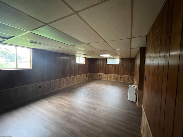 basement with wood-type flooring, wooden walls, and a drop ceiling