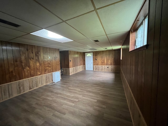 basement with a drop ceiling, wooden walls, a wealth of natural light, and hardwood / wood-style flooring