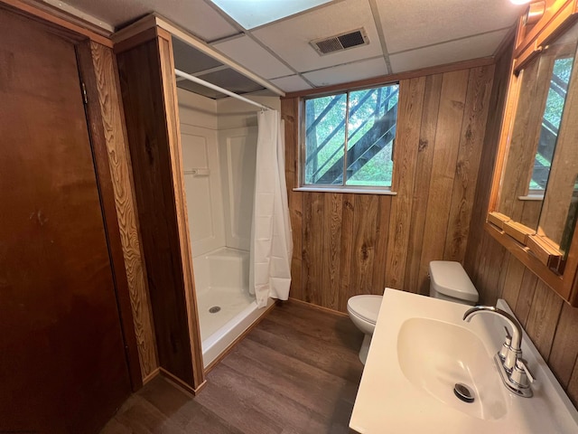 bathroom featuring wood walls, toilet, a paneled ceiling, hardwood / wood-style floors, and a shower with curtain