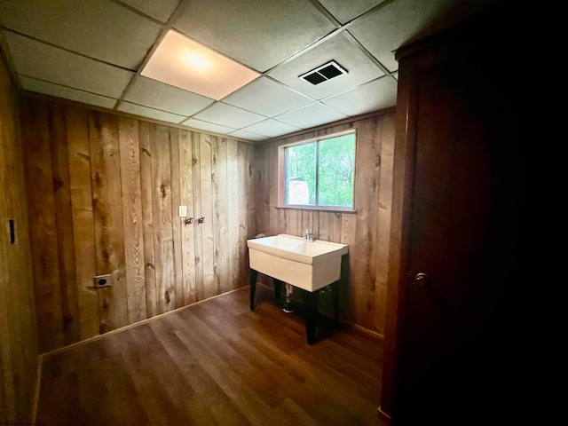 bathroom with wood-type flooring, a drop ceiling, wood walls, and sink