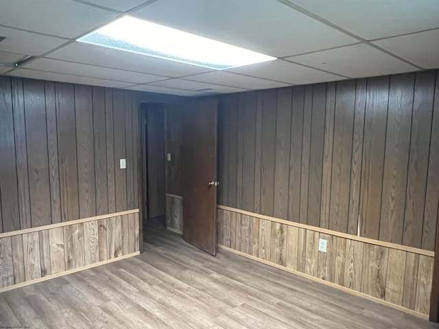 basement featuring wood-type flooring, wooden walls, and a paneled ceiling